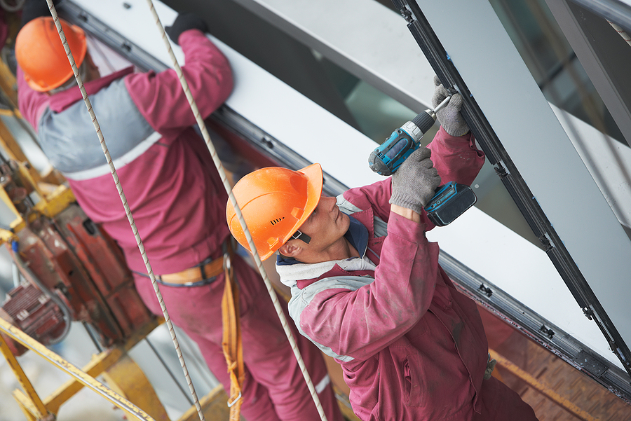 Commercial Window Installation, Two builders worker installing glass windows on facade of business building