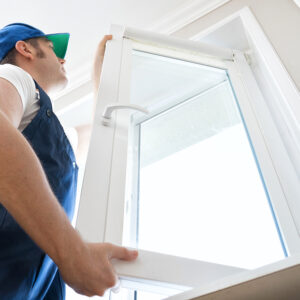 Replacement Window Installer , Professional handyman in uniform installing window at home.